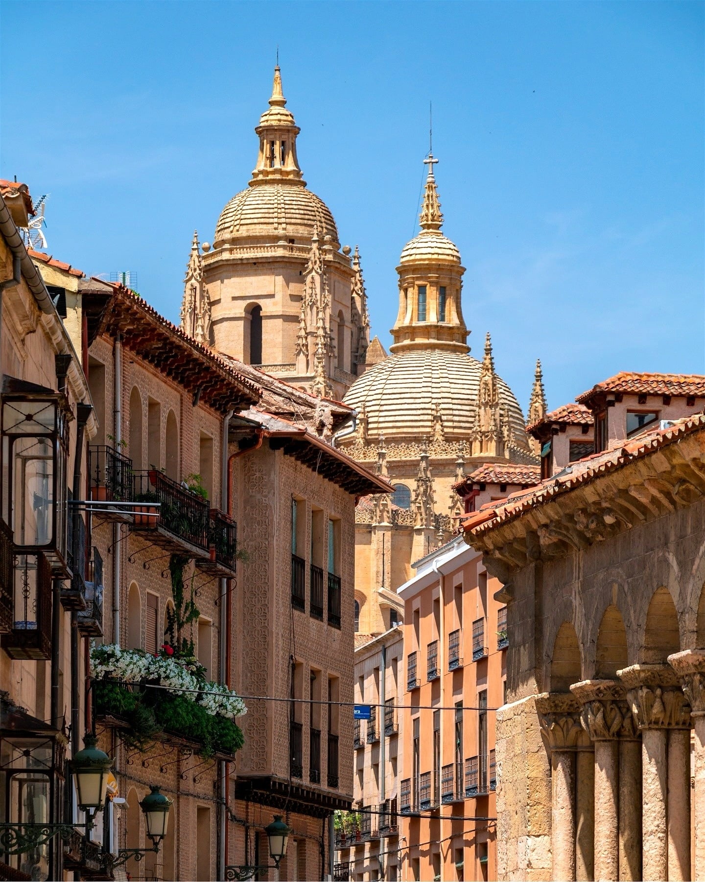 La imagen muestra el imponente acueducto romano de Segovia alzándose junto a edificios tradicionales, incluyendo el famoso Mesón Cándido con mesas al aire libre.
