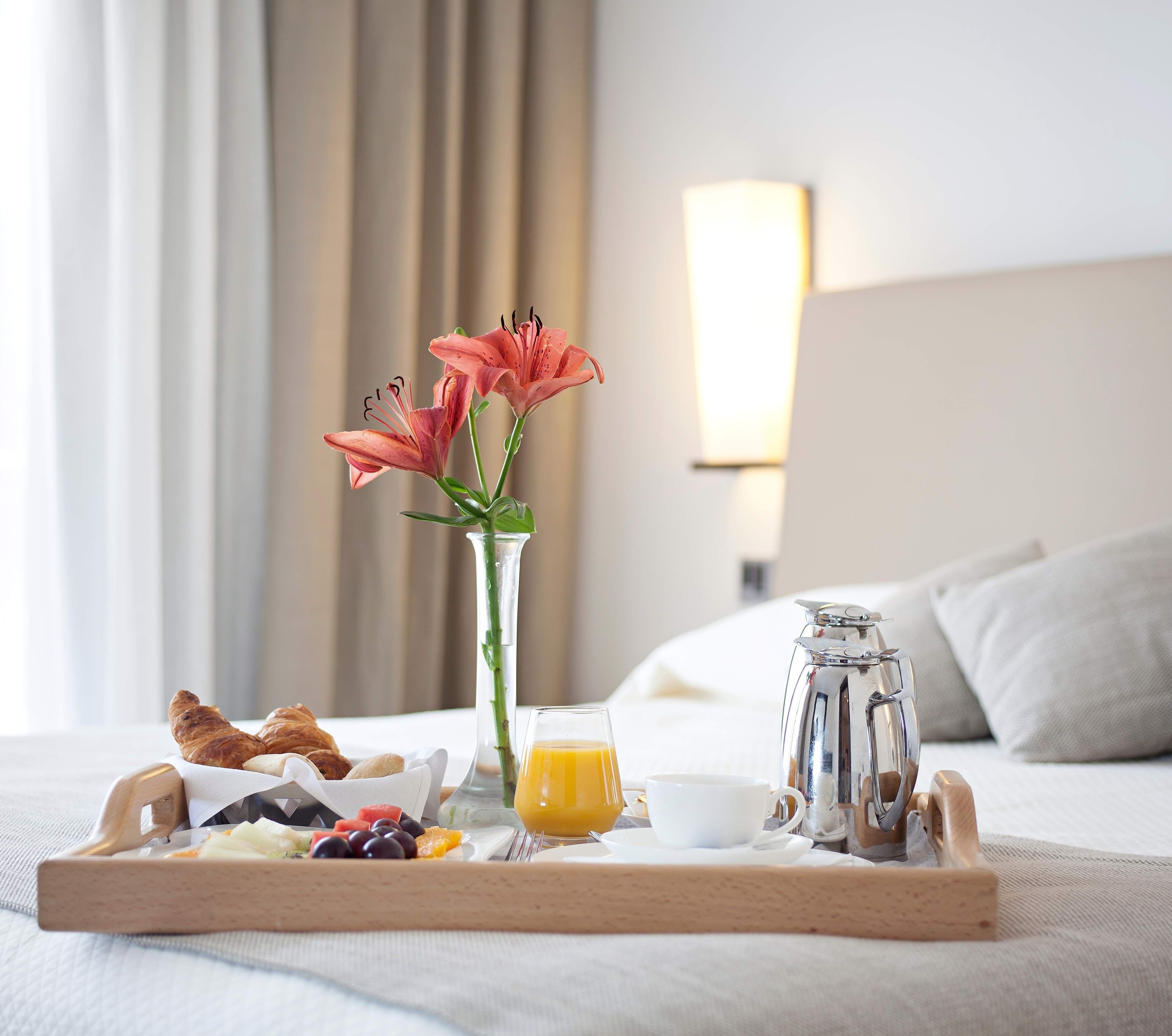 una bandeja de madera con desayuno y flores en una cama