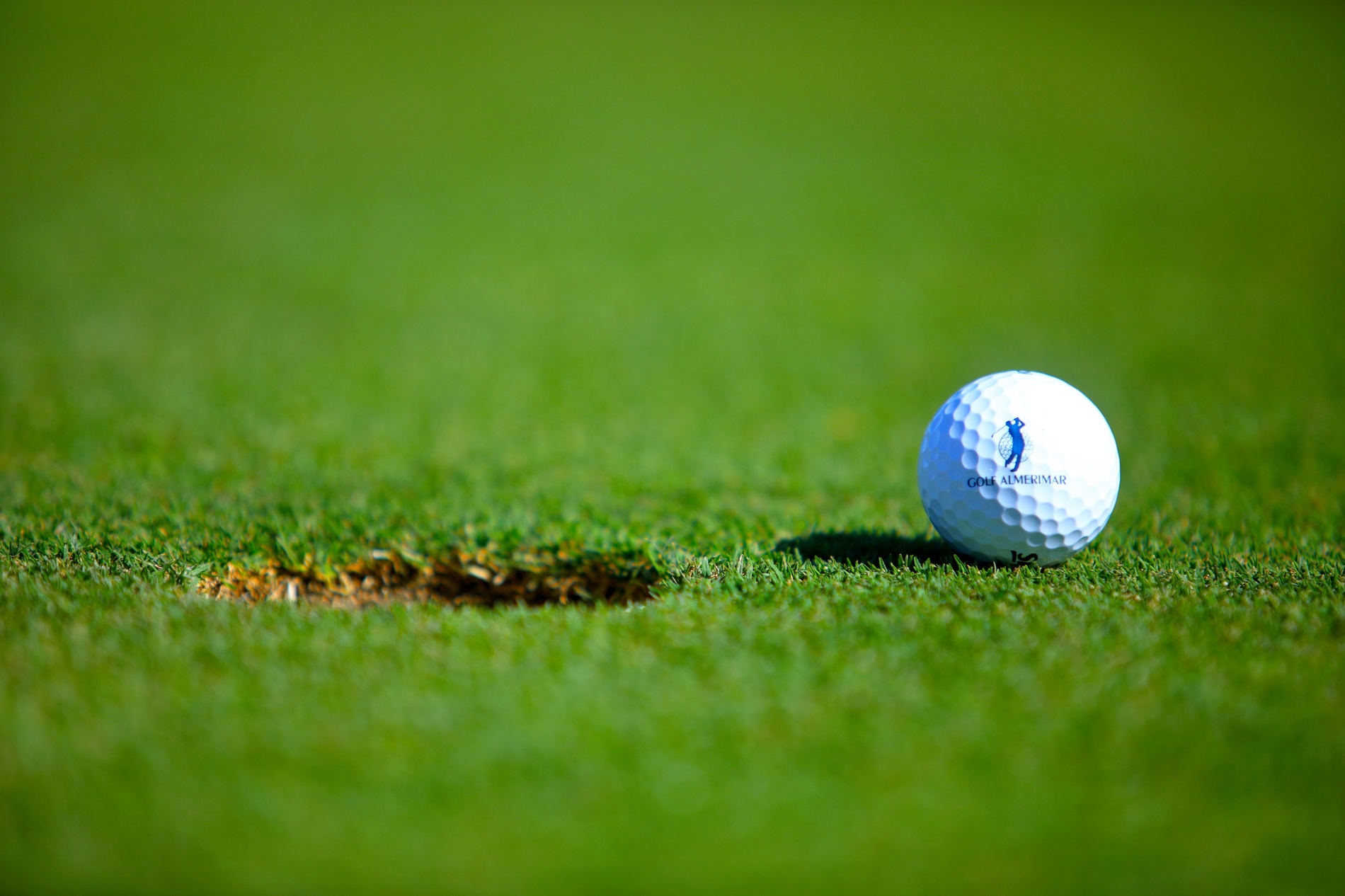Hombre jugando al golf en el campo al atardecer. Pelota cerca del hoyo. AR: Corporativa.