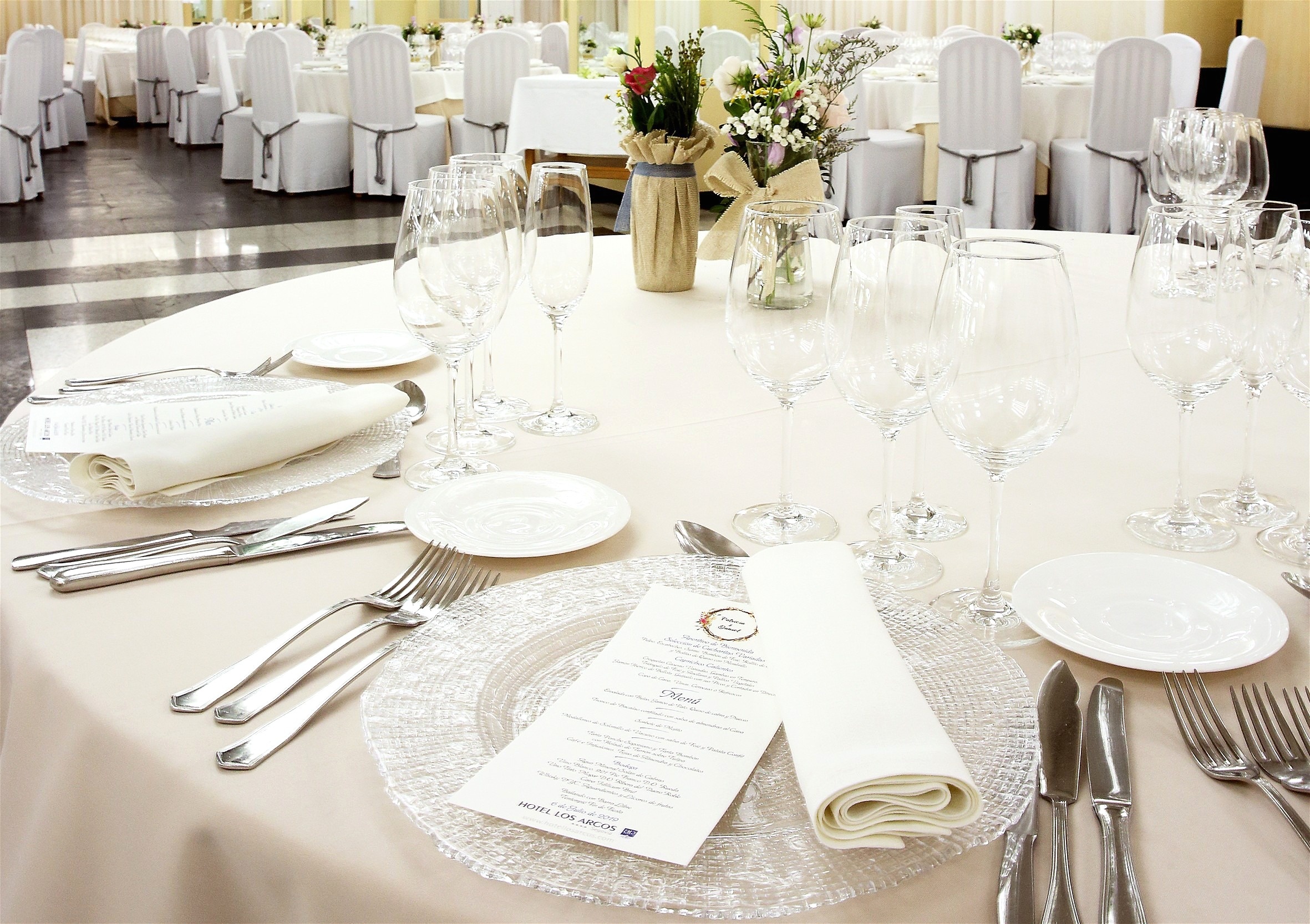 A U-shaped conference table draped in blue with white chair covers is set in a spacious room adorned with wall paintings and recessed lighting, ready for a meeting or event.