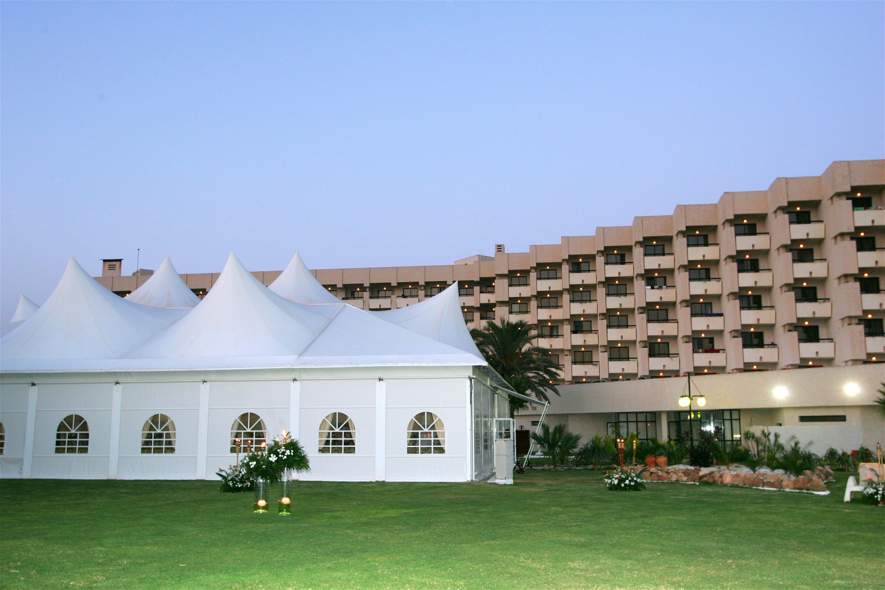 A spacious conference or event room is set up with numerous rows of dark green chairs facing a projector screen displaying the "AR HOTELES" logo and a long table at the front.