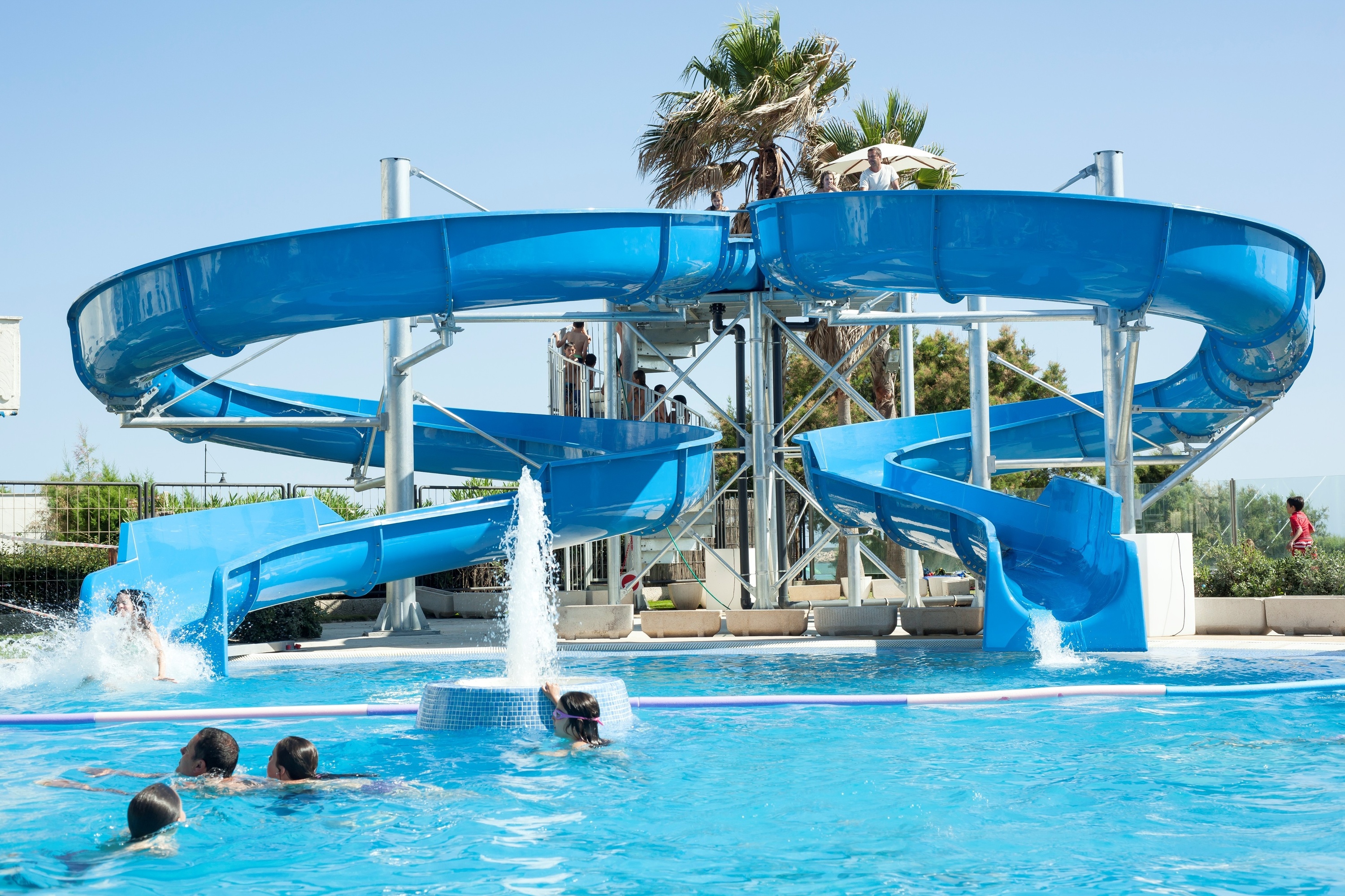 un grupo de niños nadando en una piscina junto a un tobogán azul