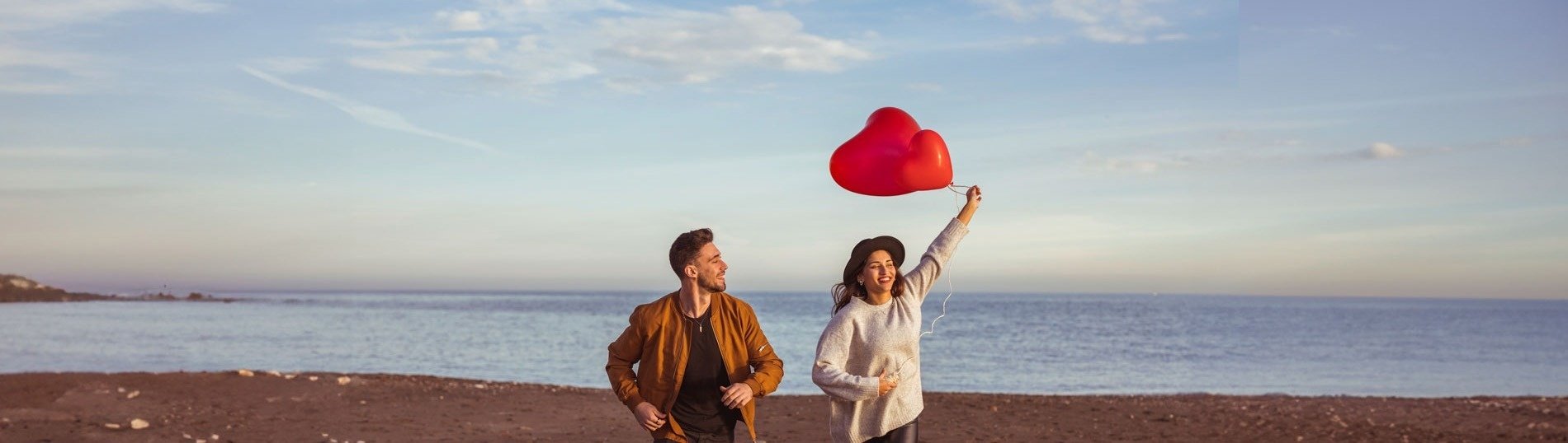 un hombre y una mujer caminan por la playa mientras la mujer sostiene un globo en forma de corazón