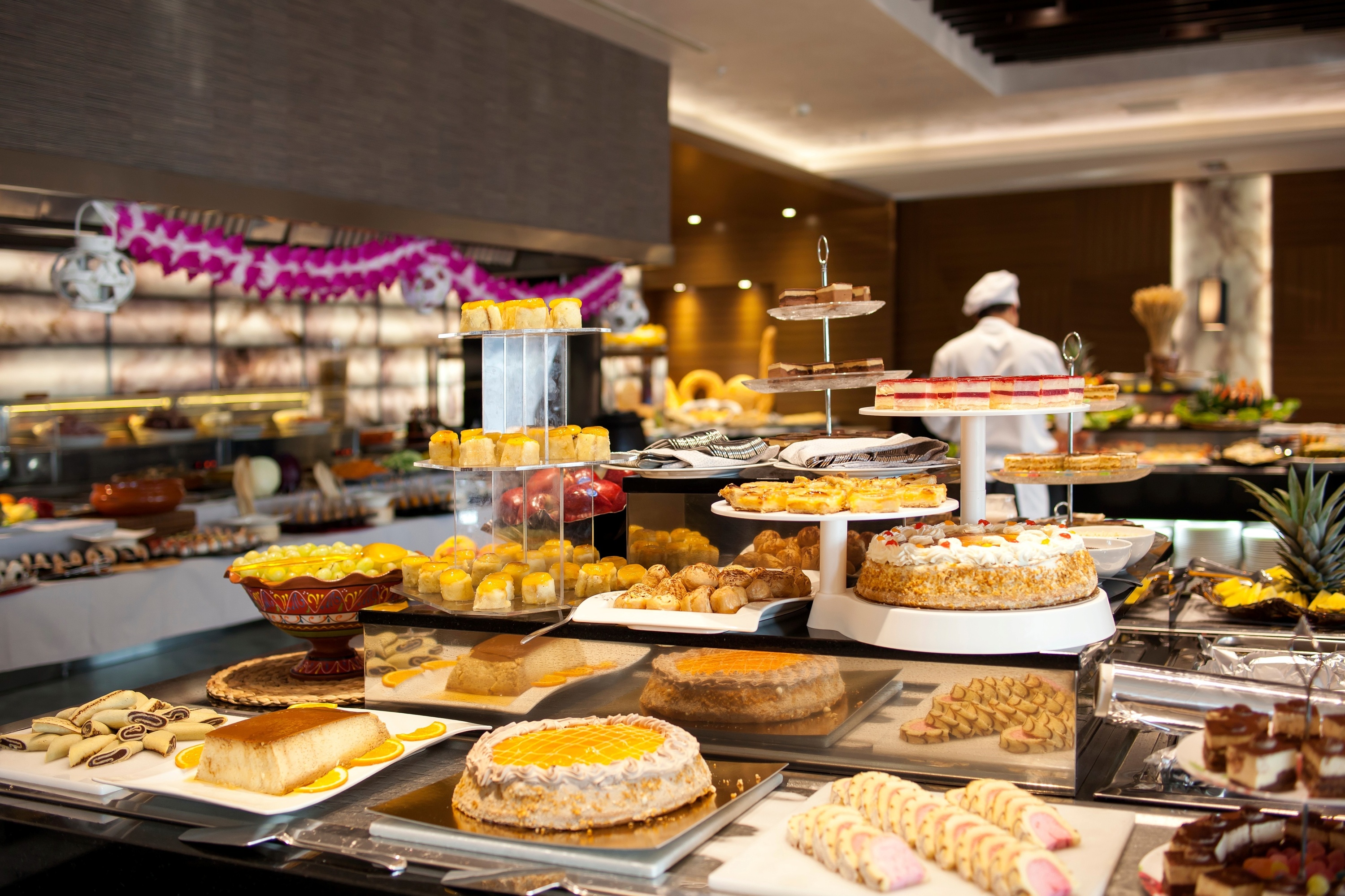 un buffet lleno de comida y pasteles con un chef en el fondo