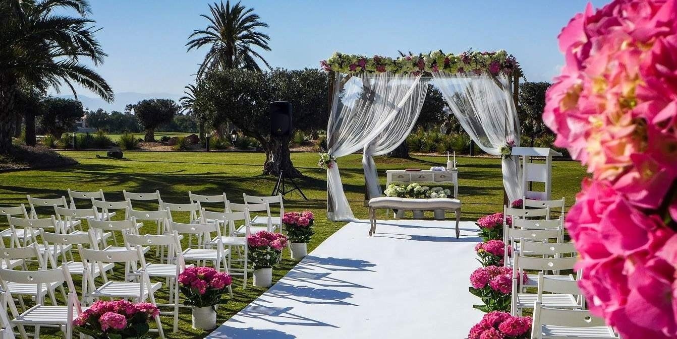 a row of white folding chairs are lined up in front of a canopy decorated with pink flowers