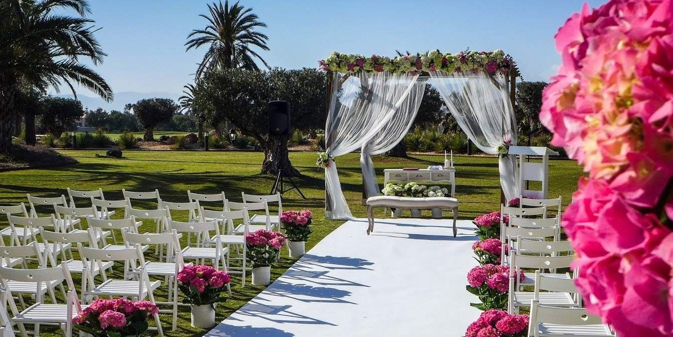 a row of white folding chairs are lined up in front of a canopy decorated with pink flowers