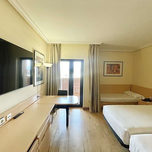 Spacious hotel room with two beds, desk, and balcony door, perfect for your AR: Parquesur getaway.