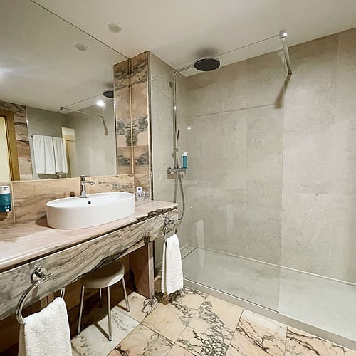 Luxurious AR: Parquesur hotel bathroom featuring marble, vanity with sink, toilet, and a bathtub with shower.