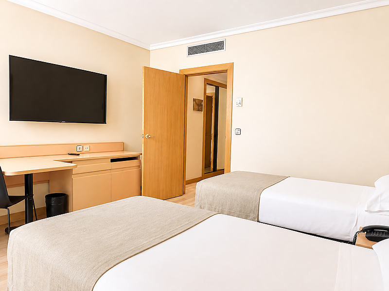 Cómoda habitación de hotel con dos camas individuales, TV y escritorio. Ideal para su estancia cerca de AR: Parquesur.