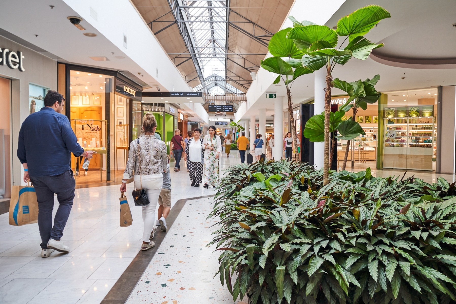 un grupo de personas caminan por un centro comercial con una tienda de perfumes en el fondo