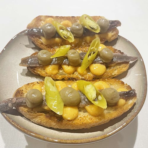 Delicious tapas AR: Parquesur with anchovies, olives, and peppers on toasted bread.