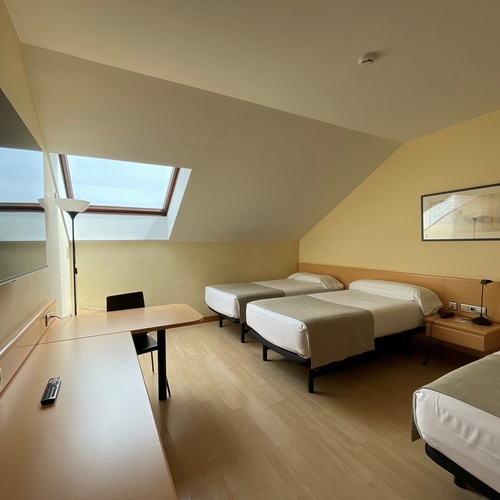 Habitación de hotel luminosa con tres camas individuales, escritorio y ventana de techo, ideal cerca de AR: Parquesur.