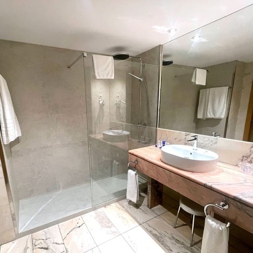 Elegante baño de hotel en AR: Parquesur con ducha de cristal, encimera de mármol y lavabo contemporáneo.