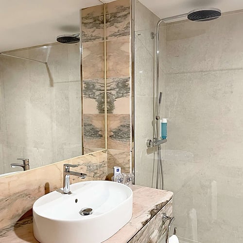 Modern hotel bathroom with double shower heads, sink, and marble counter. AR: Parquesur