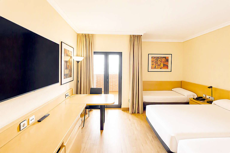 Spacious triple hotel room at AR: Parquesur with slanted ceiling, skylight, desk, and modern amenities.