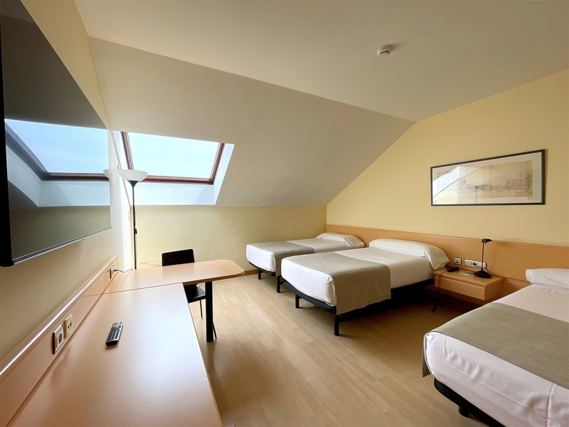 Spacious triple hotel room at AR: Parquesur with slanted ceiling, skylight, desk, and modern amenities.