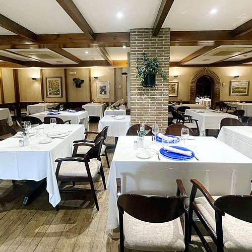 Elegant restaurant dining room with white tablecloths, dark wood chairs, and artwork. AR: Parquesur.