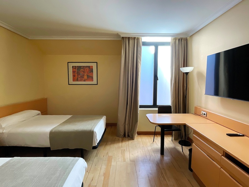 Habitación doble de hotel con dos camas, escritorio, TV y ventana, ideal para el confort de los huéspedes.