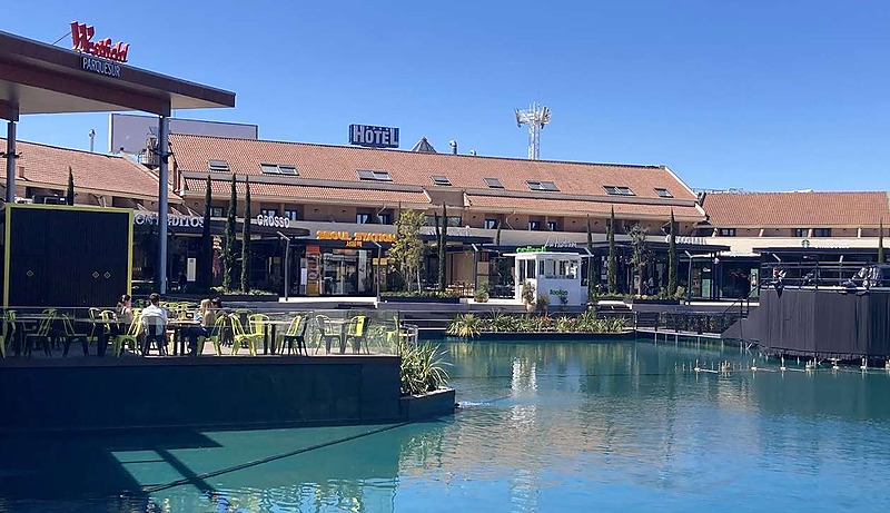 Vista exterior de Westfield Parquesur con un lago artificial turquesa, locales comerciales y pasarelas de madera.
