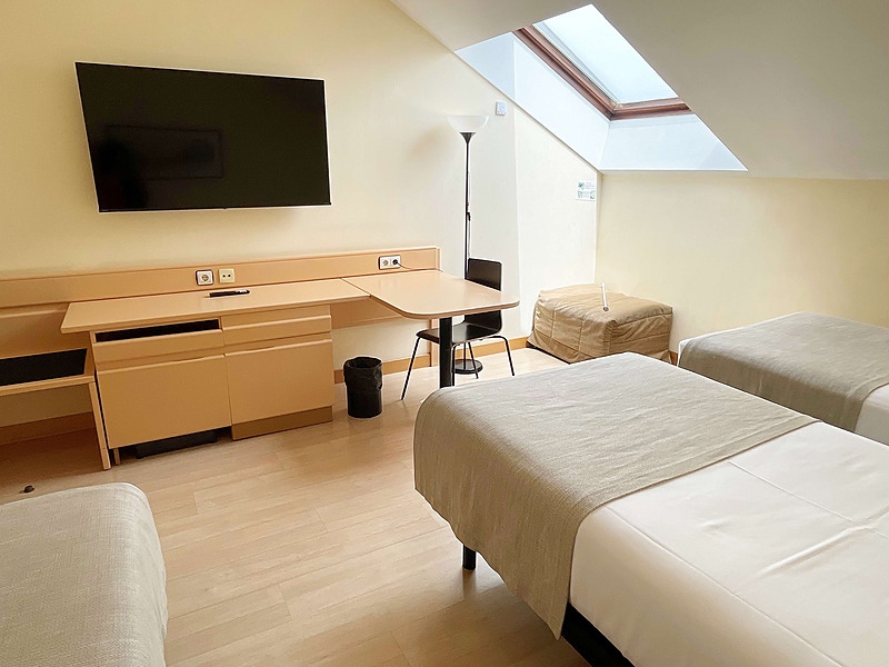 Spacious triple hotel room at AR: Parquesur with slanted ceiling, skylight, desk, and modern amenities.