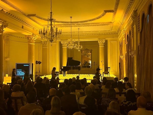 una mujer toca el piano en un gran salón lleno de gente