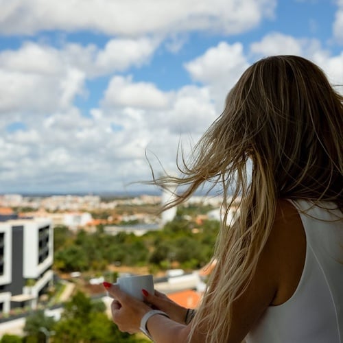a woman standing on a balcony holding a cup of coffee