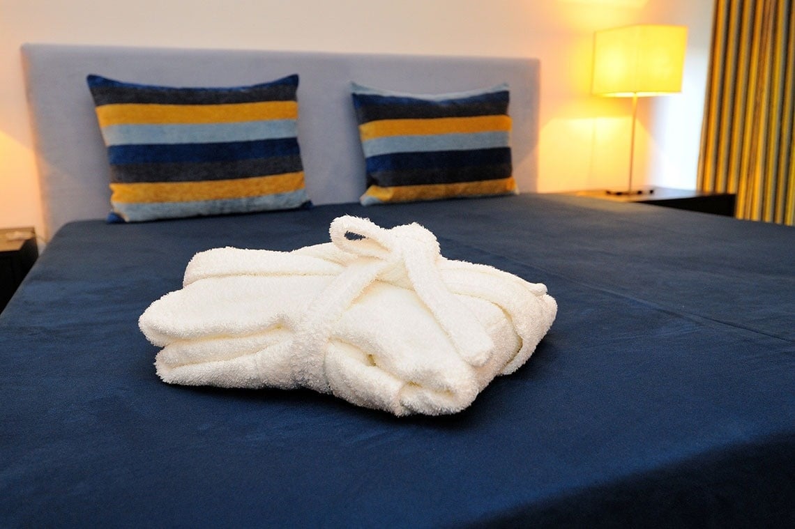 une robe blanche est posée sur un lit bleu avec des oreillers rayés