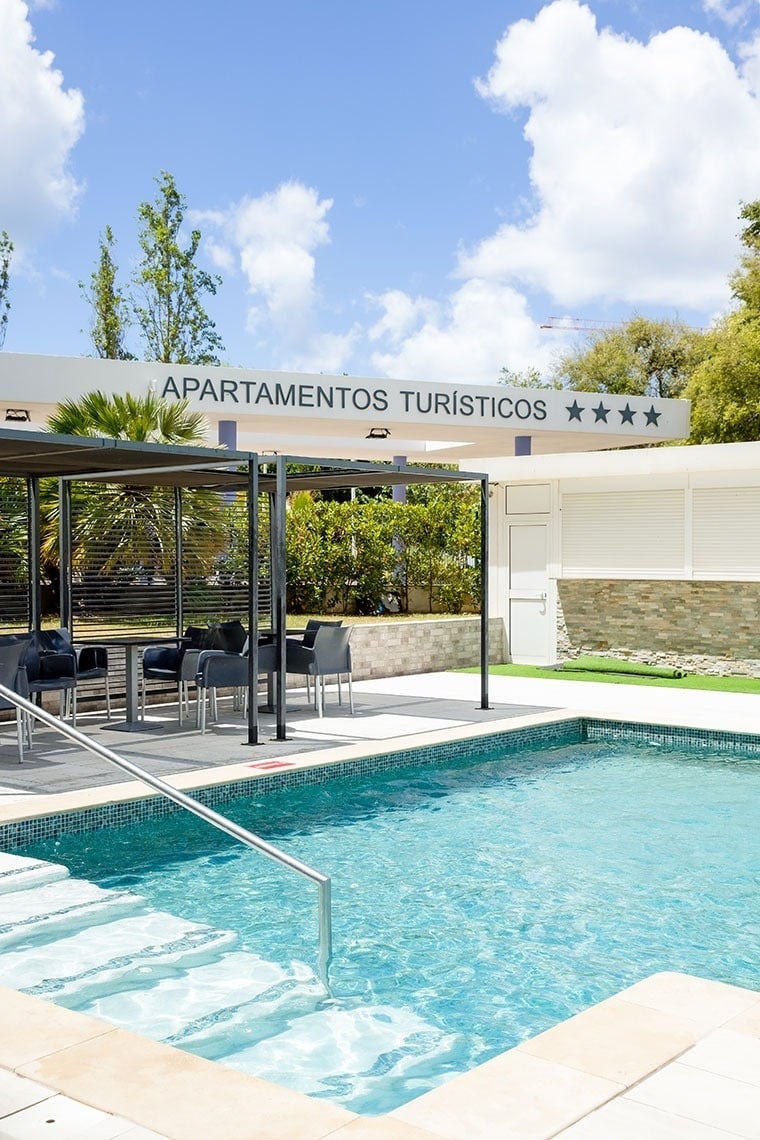 une piscine entourée de tables et de chaises sous un panneau indiquant apartamentos turisticos