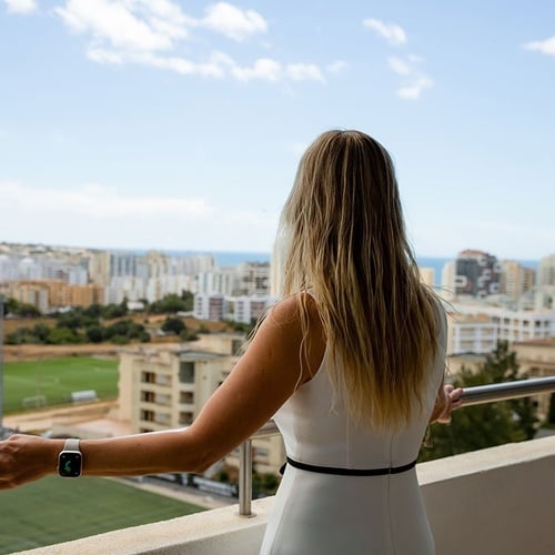 uma mulher de vestido branco está em uma varanda com vista para uma cidade