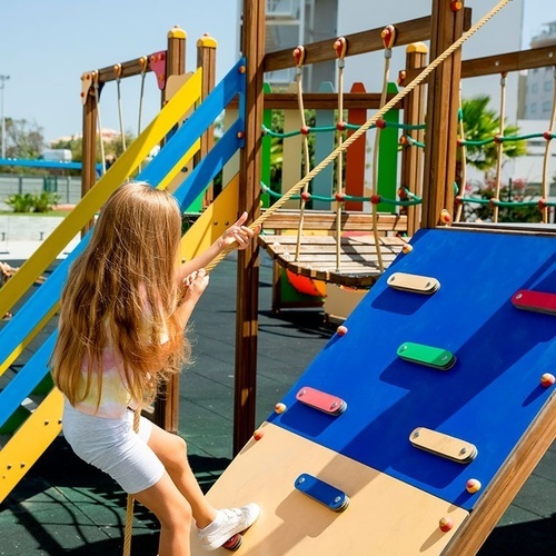 a little girl climbs a climbing wall at a playground