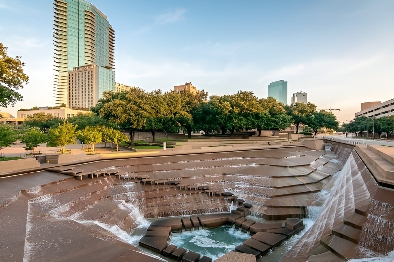 a waterfall in a park with a tall building in the background