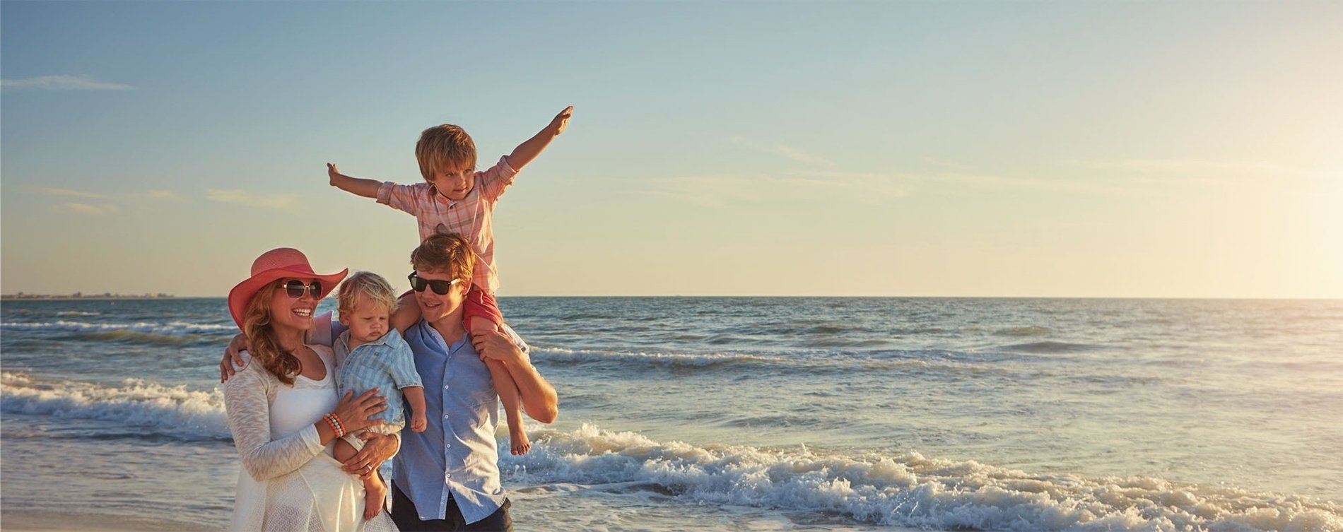 una familia camina por la playa con dos niños en los hombros