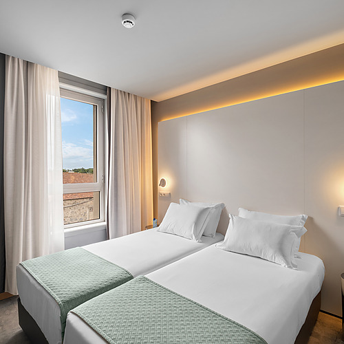 Habitación moderna con dos camas individuales, ventana y luz ambiental, ideal para Axis: Corporate.