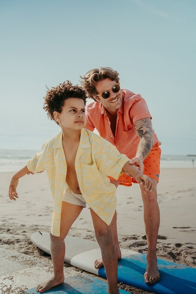 um homem e um menino estão em uma prancha de surf na praia
