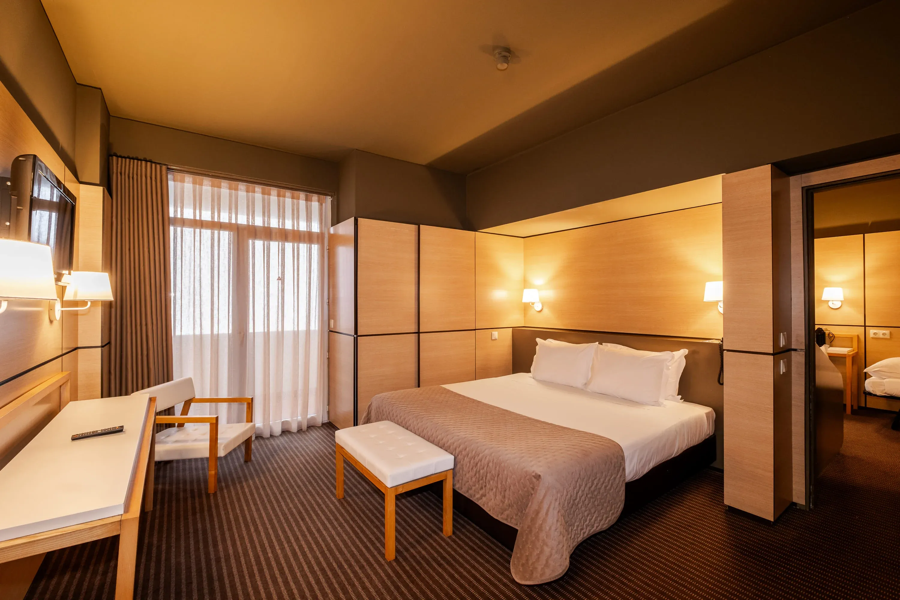 Quarto de hotel confortável com Vermar | Axis Hotéis & Golfe | Website Oficial: cama, luminária, mesa de cabeceira e janela com cortinas.