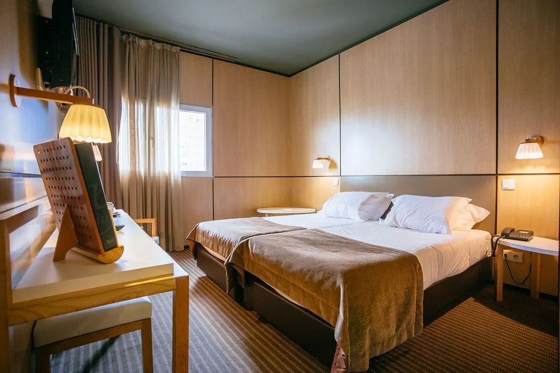Quarto duplo com duas camas confortáveis, decoração moderna e janela em hotel Vermar | Axis Hotéis & Golfe | Website Oficial.