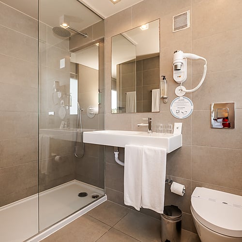 Baño moderno y espacioso con ducha, lavabo, inodoro y secador de pelo. Axis: Corporate