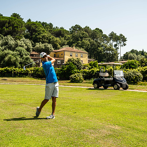 Golfista haciendo un swing en un campo de golf con un carrito de golf al fondo, un hotel Axis: Corporate perfecto.