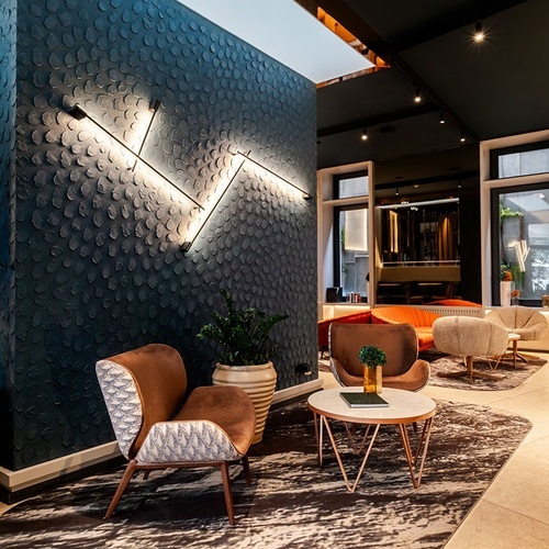 A chic lounge area features a textured dark teal wall with striking linear lighting, complemented by comfortable brown armchairs and a patterned rug.