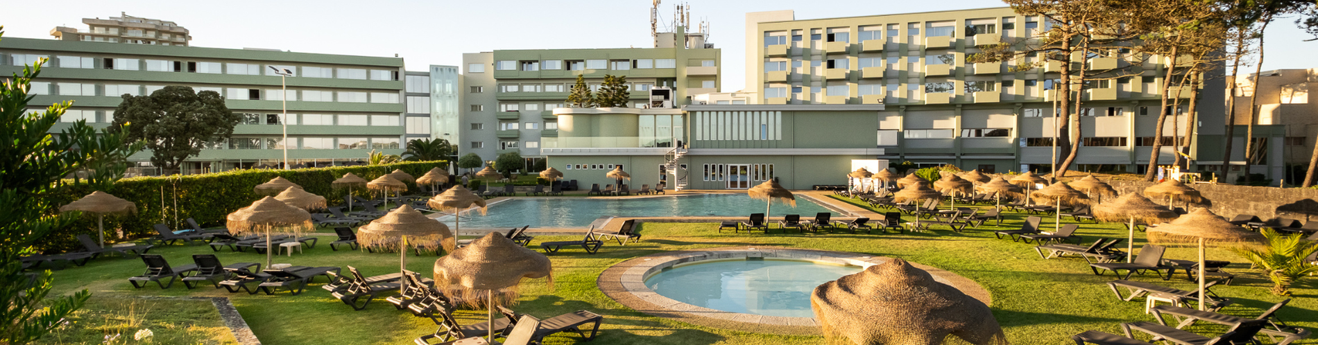Hotel moderno com piscina exterior, espreguiçadeiras, guarda-sóis e jardim, perfeito para relaxar.