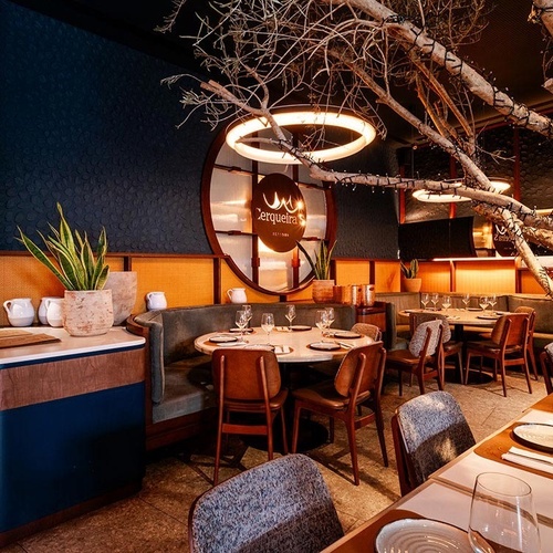 This image captures the interior of a stylish restaurant or bar, featuring a blend of dark blue and orange hues, banquette seating, and a large, illuminated decorative tree at its center.