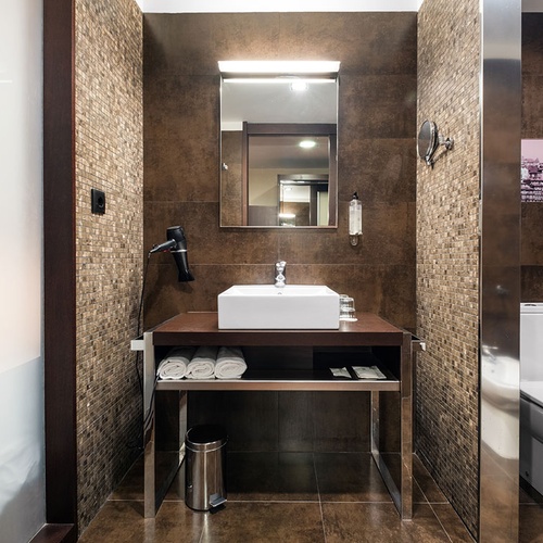 Moderna casa de banho em tons terrosos, equipada com lavatório, espelho, sanita e parte de um duche.