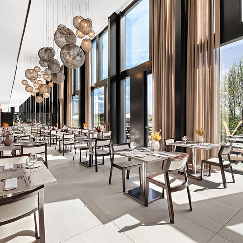 Um restaurante moderno e espaçoso com grandes janelas que oferecem vistas para o exterior, mesas postas e luminárias esféricas suspensas.