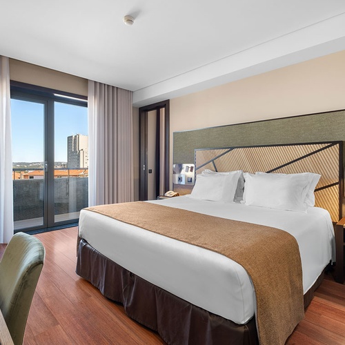 Um quarto de hotel moderno com uma cama grande, piso de madeira e uma varanda com vista para a cidade.