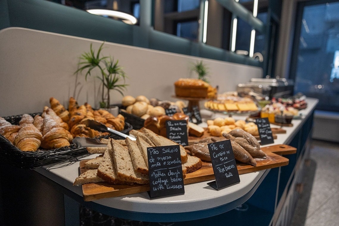 une table remplie de pains et de croissants avec des plaques de pain écrites en portugais