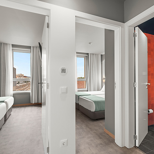 Habitación doble con dos camas, baño con azulejos naranjas y vistas a las vías del tren. Axis: Corporate