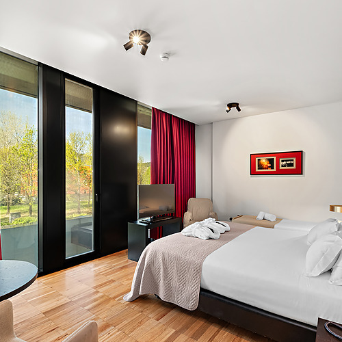 Quarto de hotel com varanda, vista para árvores, TV, roupões e duas camas. Axis: Corporate