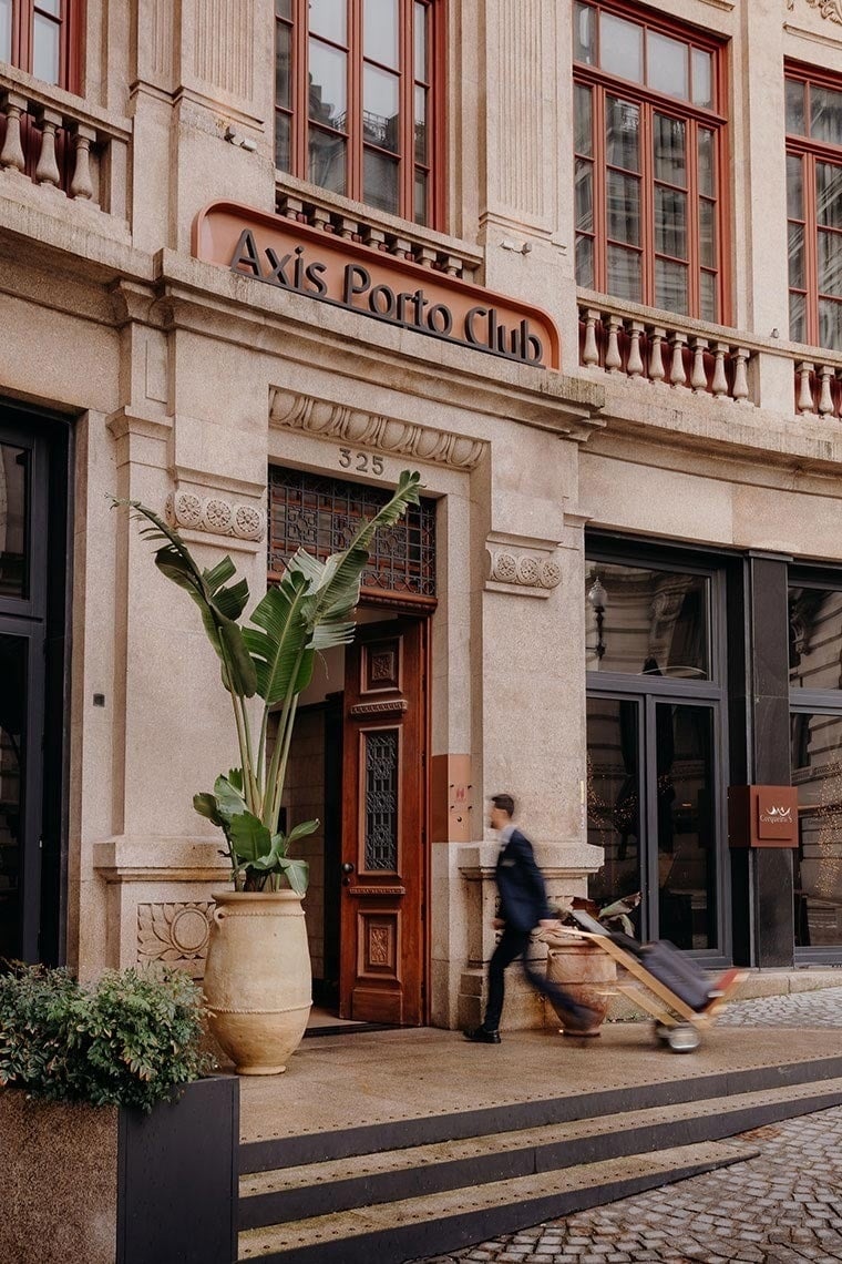 Um homem puxa a sua bagagem em frente à entrada de um edifício com a placa 