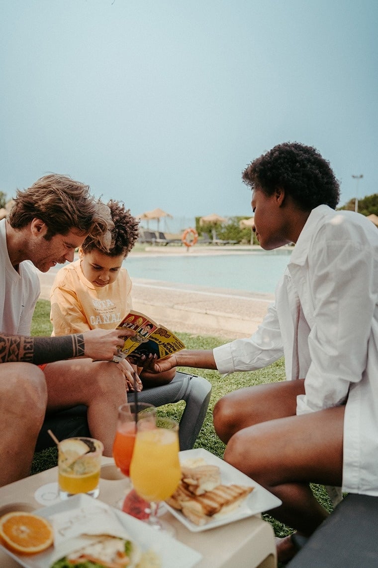 um menino está lendo uma revista enquanto um homem e uma mulher olham para ele