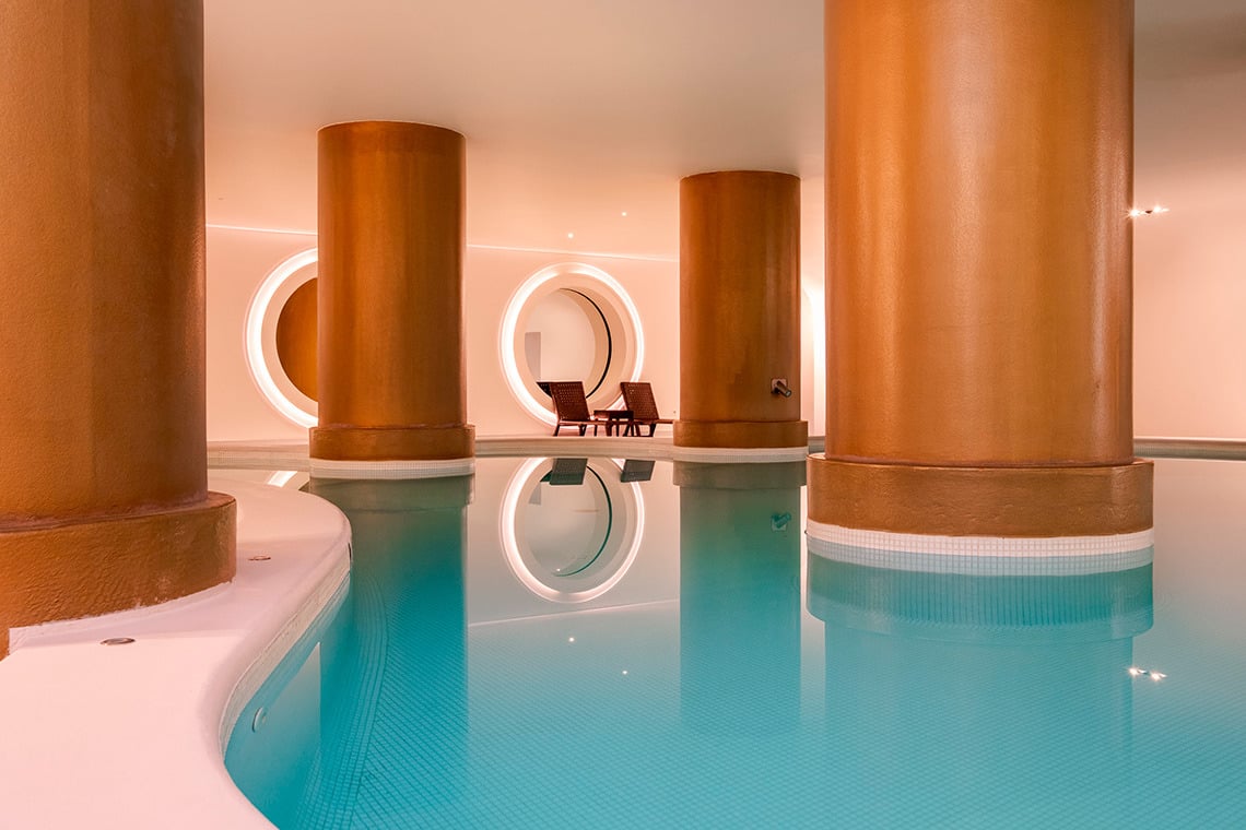 Piscina interior de hotel con columnas doradas y tumbonas. Vermar | Axis Hotéis & Golfe | Web Oficial de lujo.